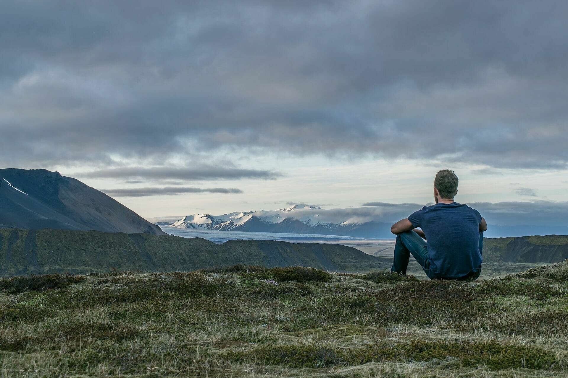 Junger Mann sitzt auf einem Berghügel und blickt über Berge