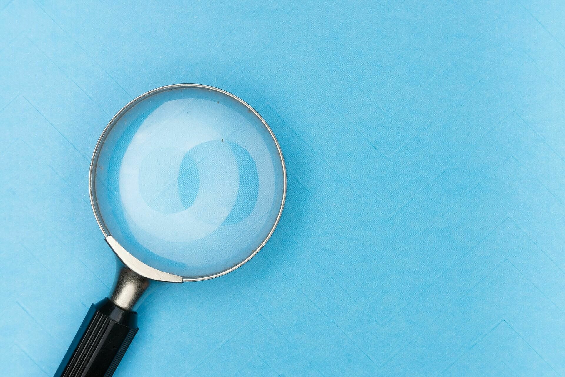 Eine Lupe auf einem tyrkis-blauen, flachen Hintergrund
